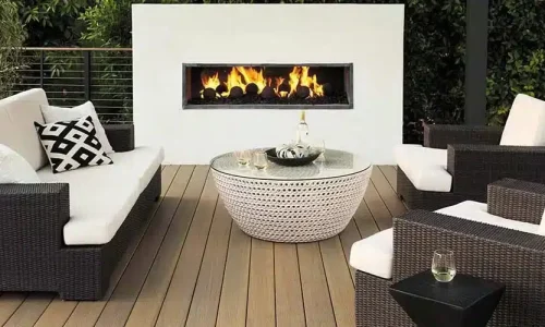 A built-in outdoor fire place is lit on a medium brown deck